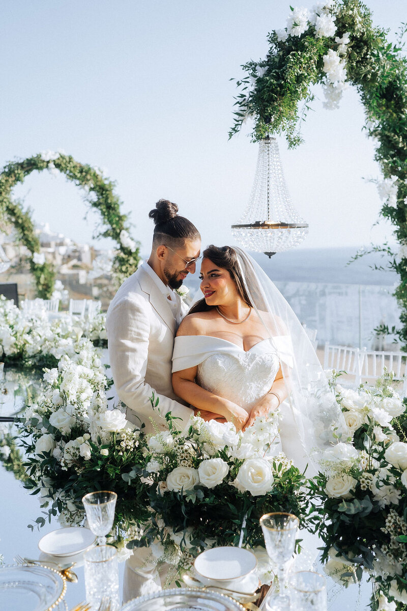 Luxury Mykonos wedding couple portrait surrounded by elegant white floral arrangements and romantic reception décor overlooking the sea during a destination wedding in Mykonos
