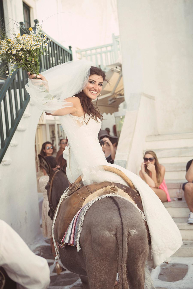 A bride joyfully rides a donkey during a traditional wedding in Mykonos, a picturesque destination.