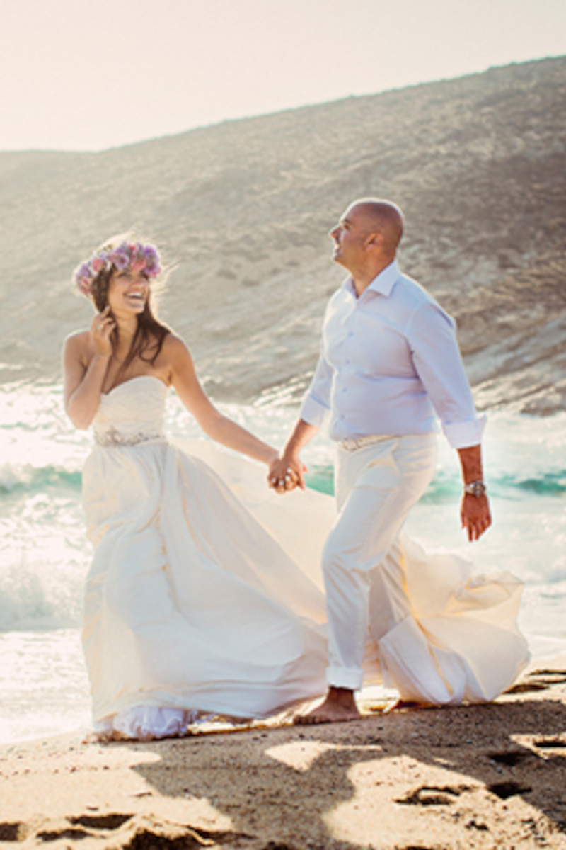 A beautiful bride and groom walking hand in hand on the sandy beach during their beach destination wedding in Mykonos.