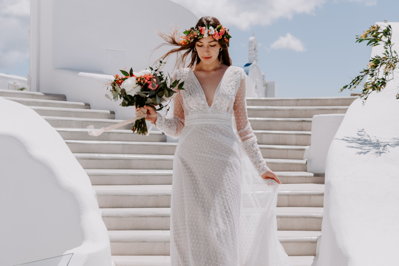 Bride in white dress on steps of white building for Mykonos wedding planning, indicating the planning steps process. 