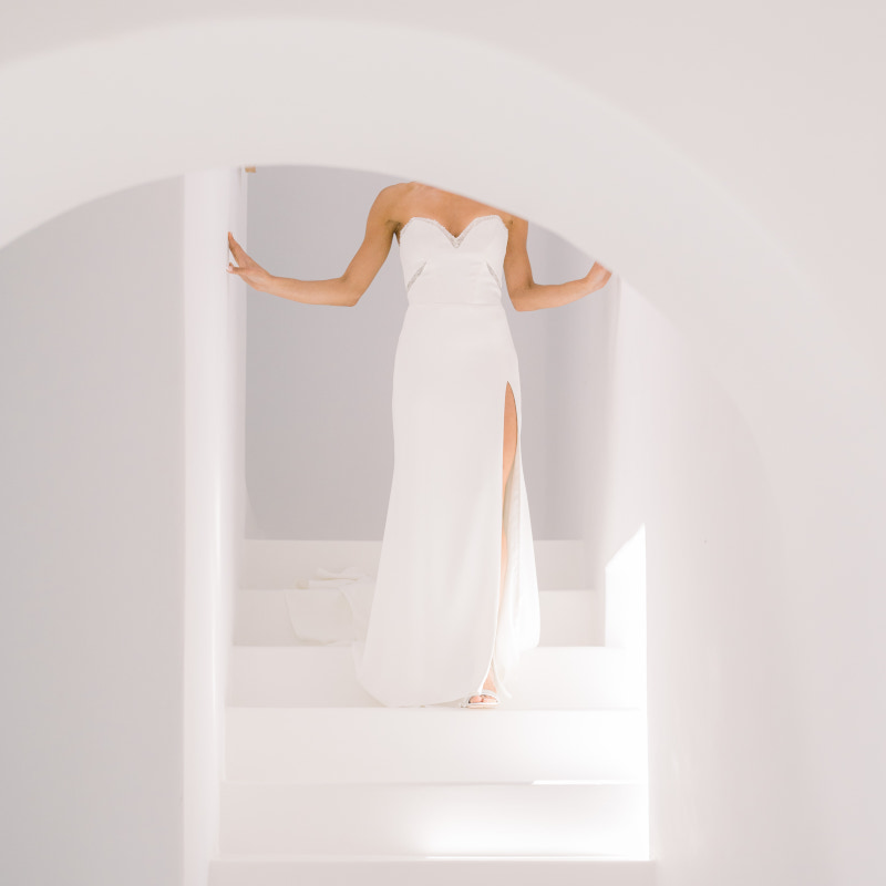 Elegant bride poses on Mykonos stairway in white dress, a sample of Mykonos wedding portfolio. 