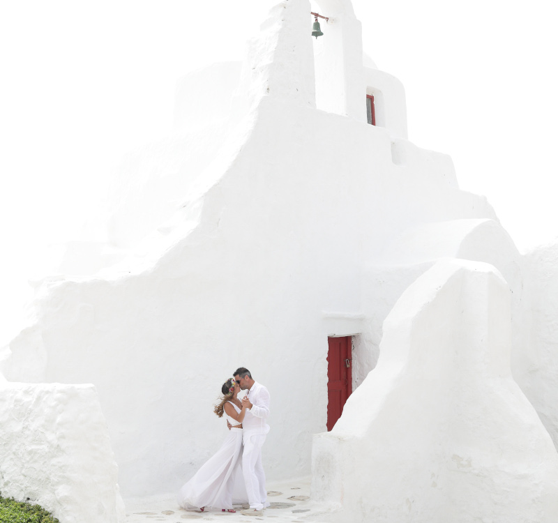A couple kissing in a white washed chapel of paraportiani in Mykonos, this is why you should choose Mykonos as your wedding destination.